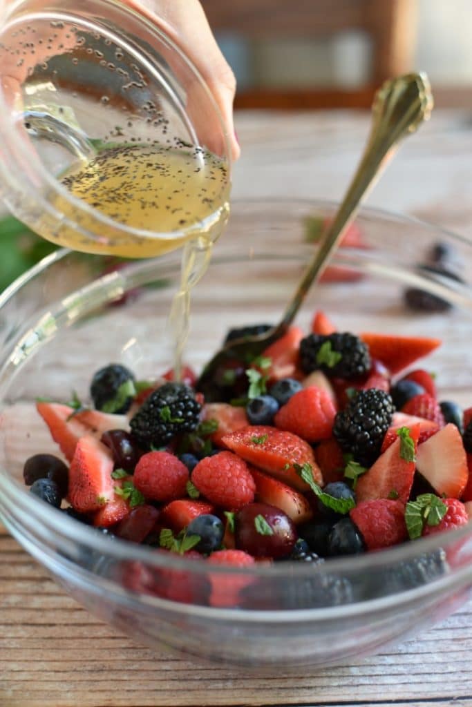 pouring mint lime dressing onto mixed berries in bowl