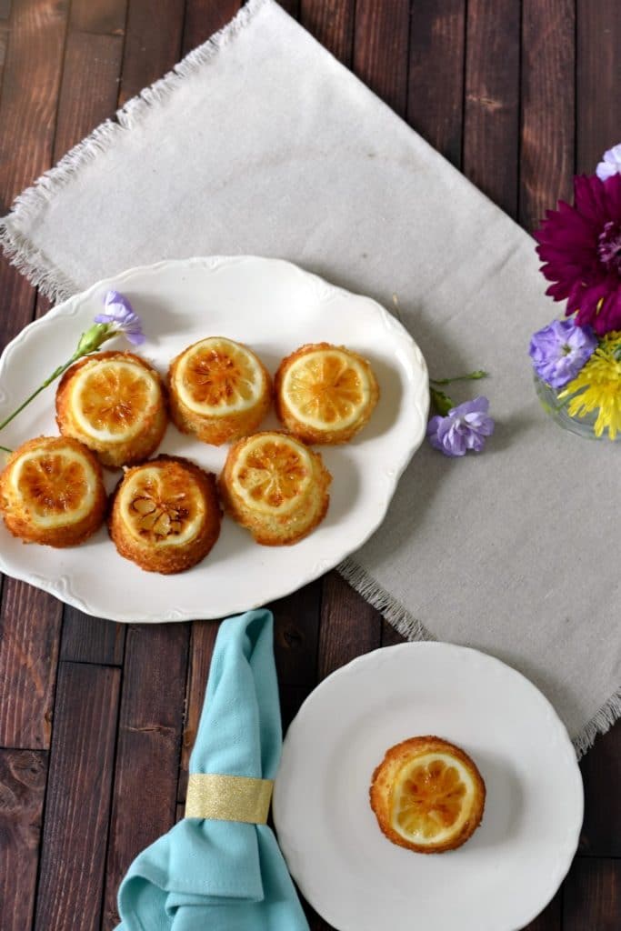 Two plates of lemon cakes on a wooden table with napkins and flowers