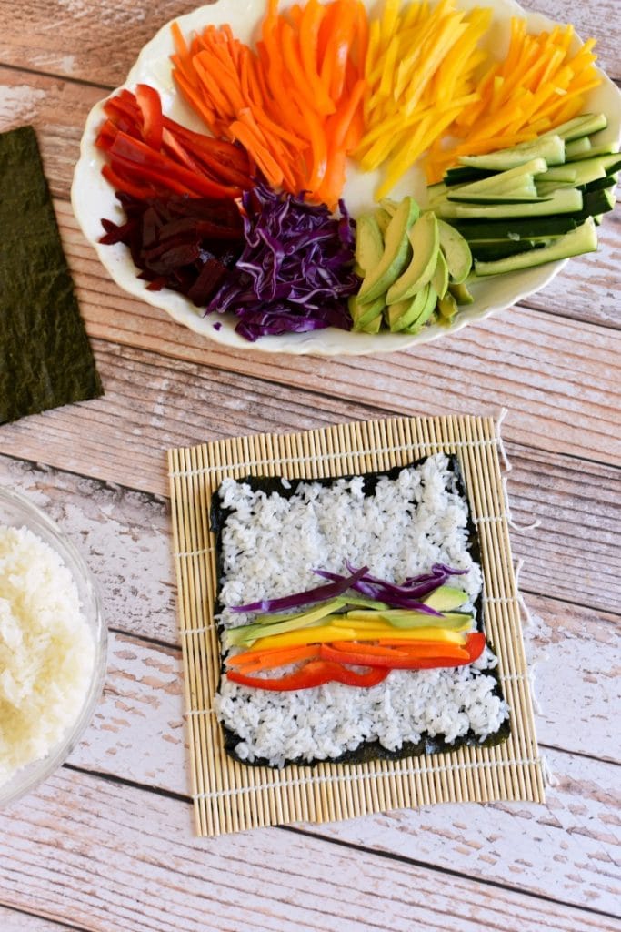 A platter of rainbow veggies and a sushi mat with an unrolled veggie sushi