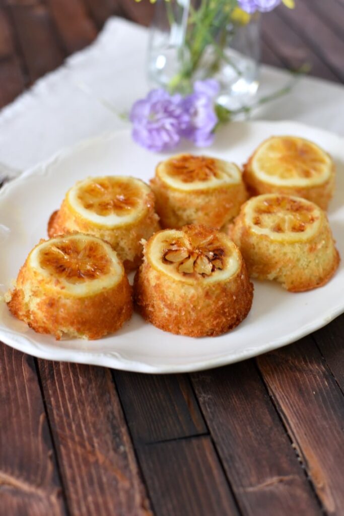 A serving platter with lemon cakes and flowers on a wooden table