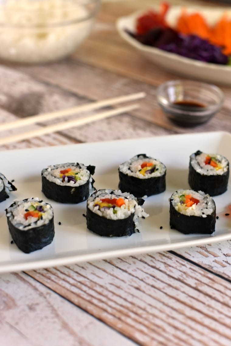 A white rectangular plate with rainbow veggie sushi