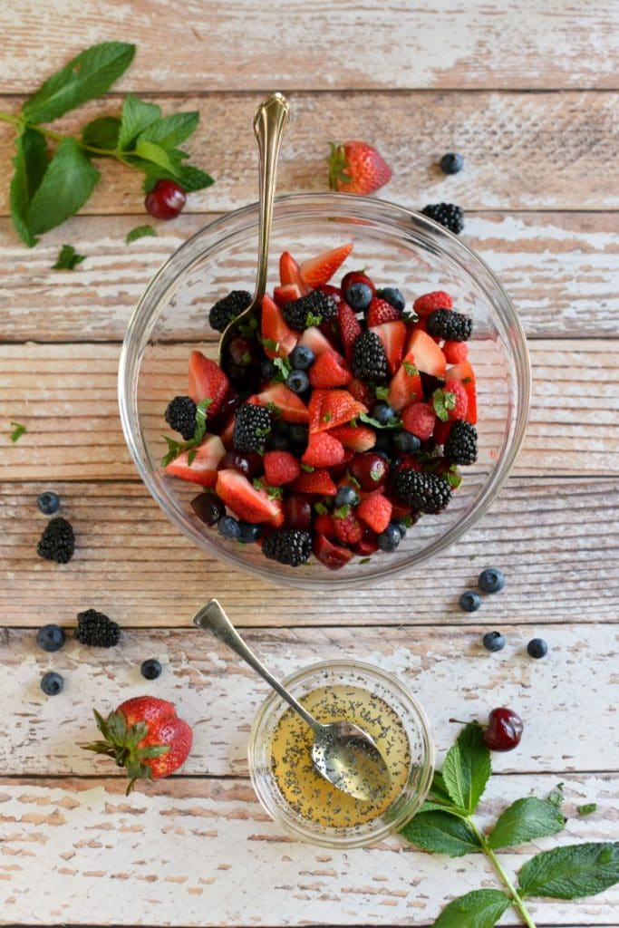 A clear serving bowl of berries and a clear pinch bowl of honey poppy seed dressing 