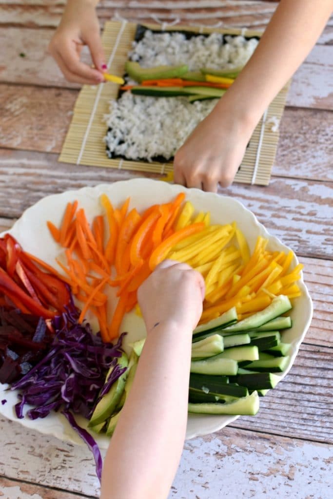 Two children making rainbow veggie sushi