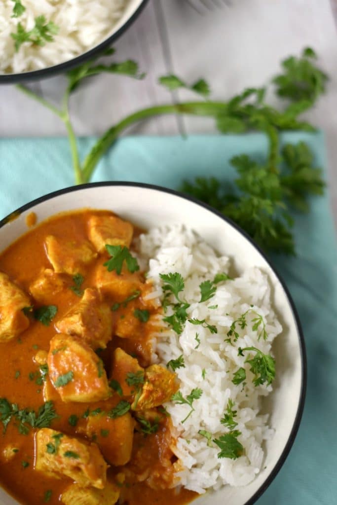 A bowl of chicken tikka masala on a blue napkin with fresh cilantro 