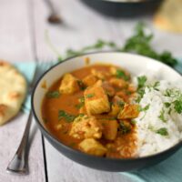 A bowl of chicken tikka masala with rice on a wooden table
