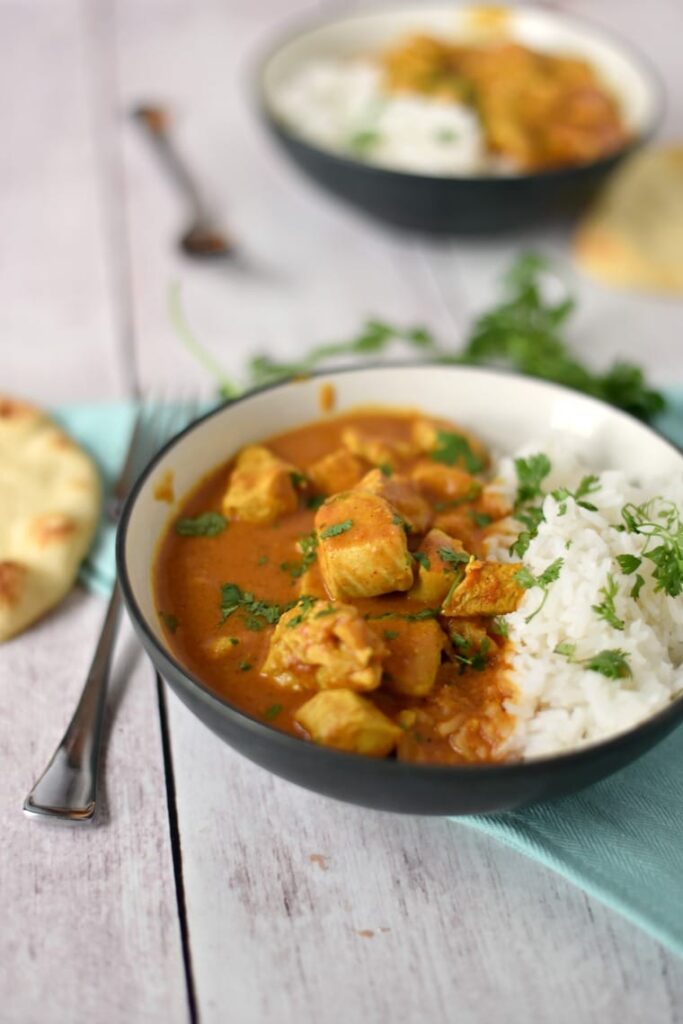 A bowl of chicken tikka masala with rice on a wooden table