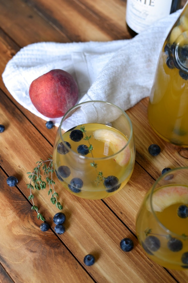 Chardonnay Summer Sangria in glass on table surrounded by peach and blueberries
