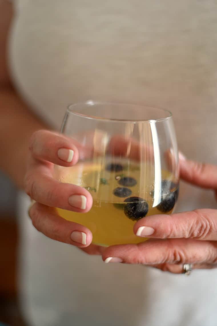hand holding glass of peach sangria with blueberries in it