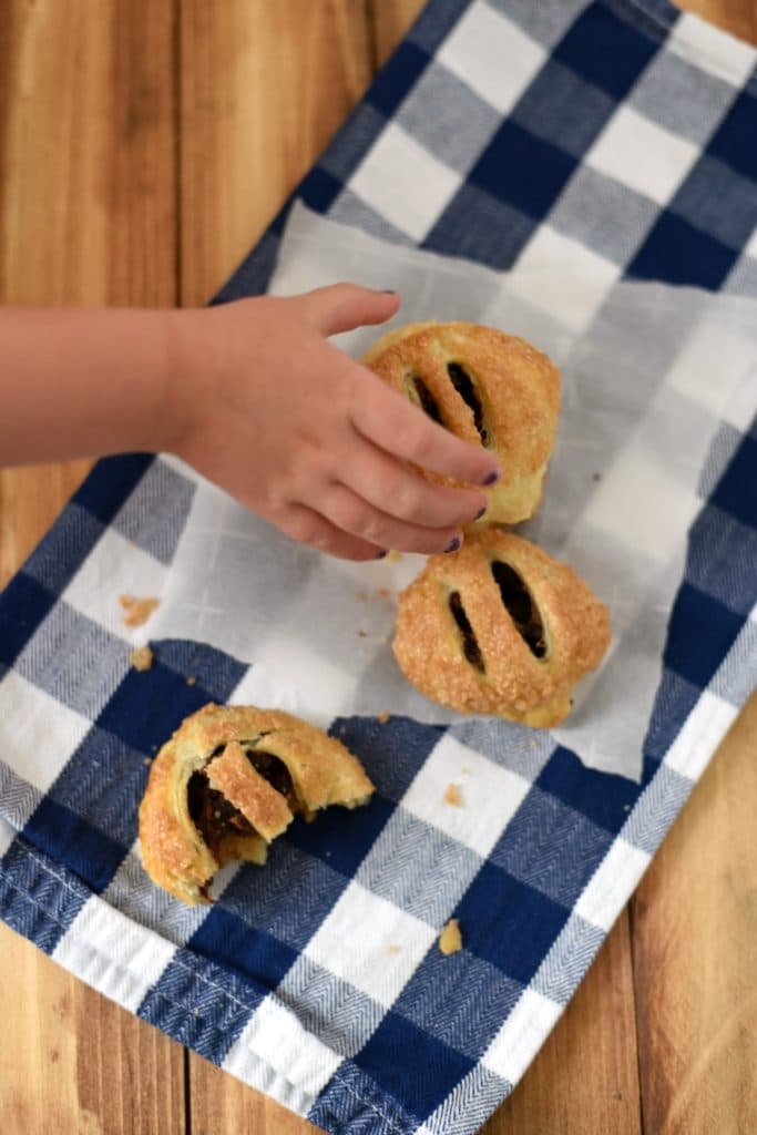 A child reaching for three cauldron cakes on a white and blue napkin