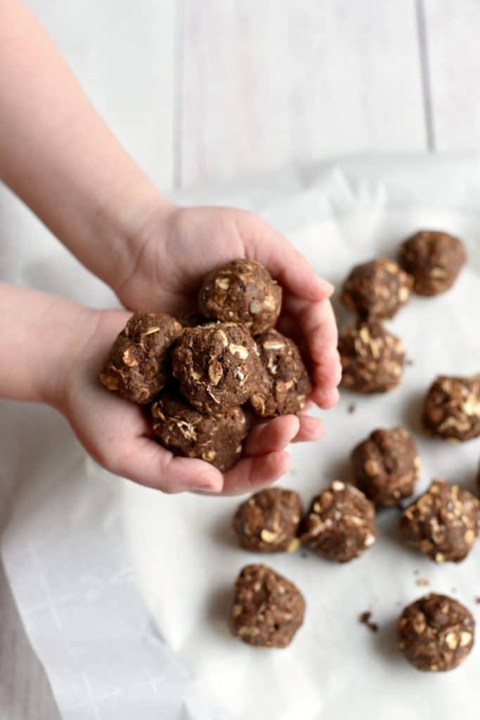 A child holding chocolate peanut energy balls over a white plate 