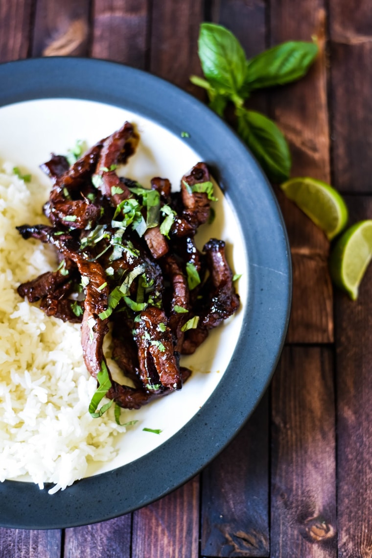 a plate with rice and Korean beef bulgogi on a wooden table with herbs and limes 