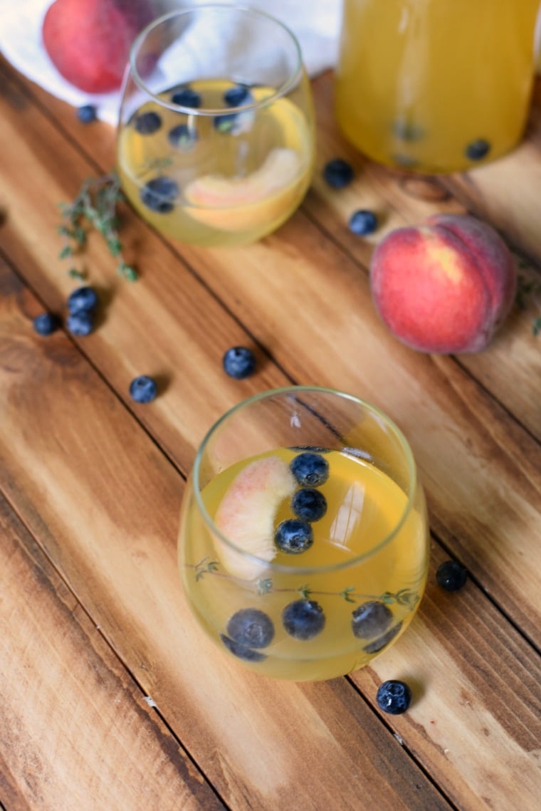 glasses of peach sangria with blueberries on table with pitcher and bottle of chardonnay