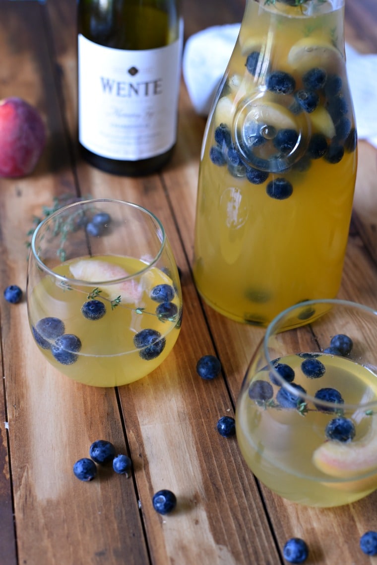 glasses of chardonnay sangria with peaches and blueberries by pitcher