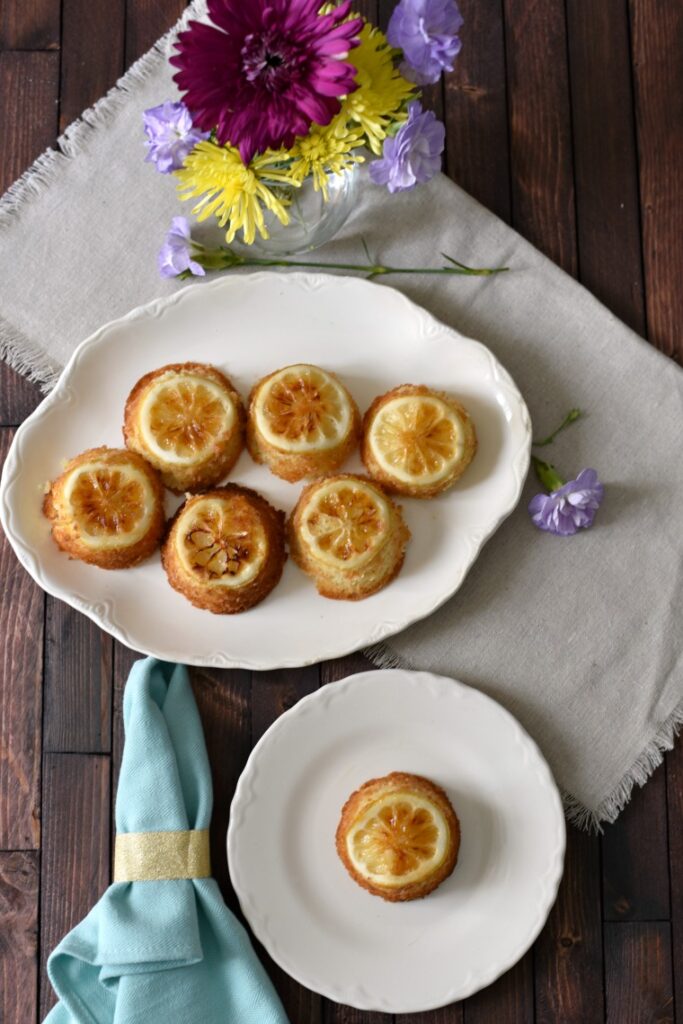 Two white plates with lemon cakes on a wooden table with scattered flowers 
