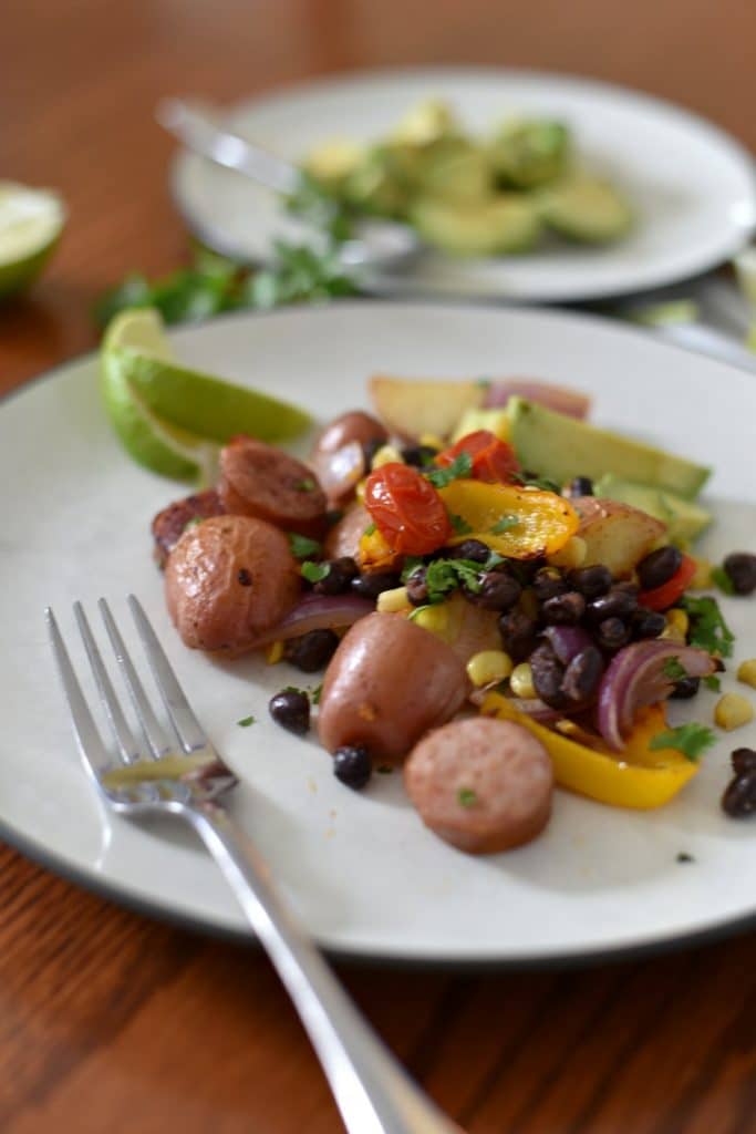 A white plate of sausage sheet pan dinner with a silver fork