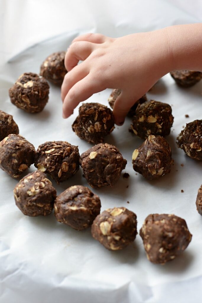 A child reaching for a plate of chocolate peanut butter energy balls 