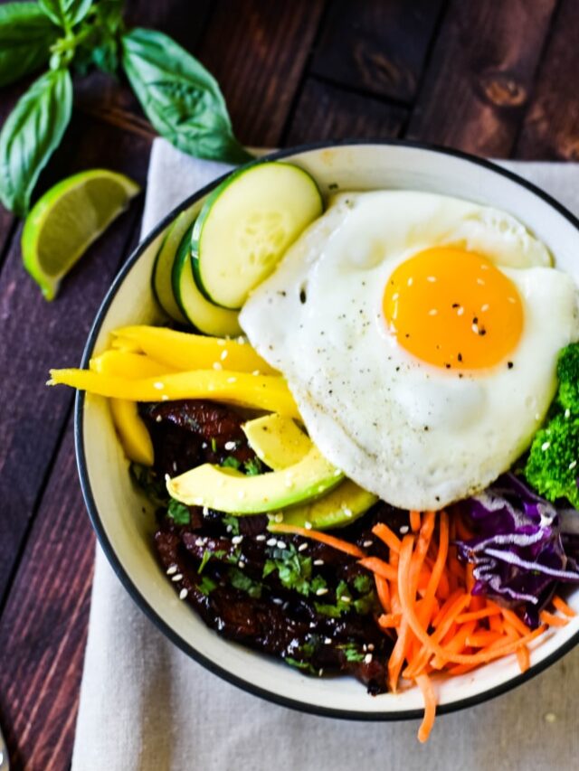 A bowl of Korean beef bulgogi on a wooden table and white napkin with a silver fork