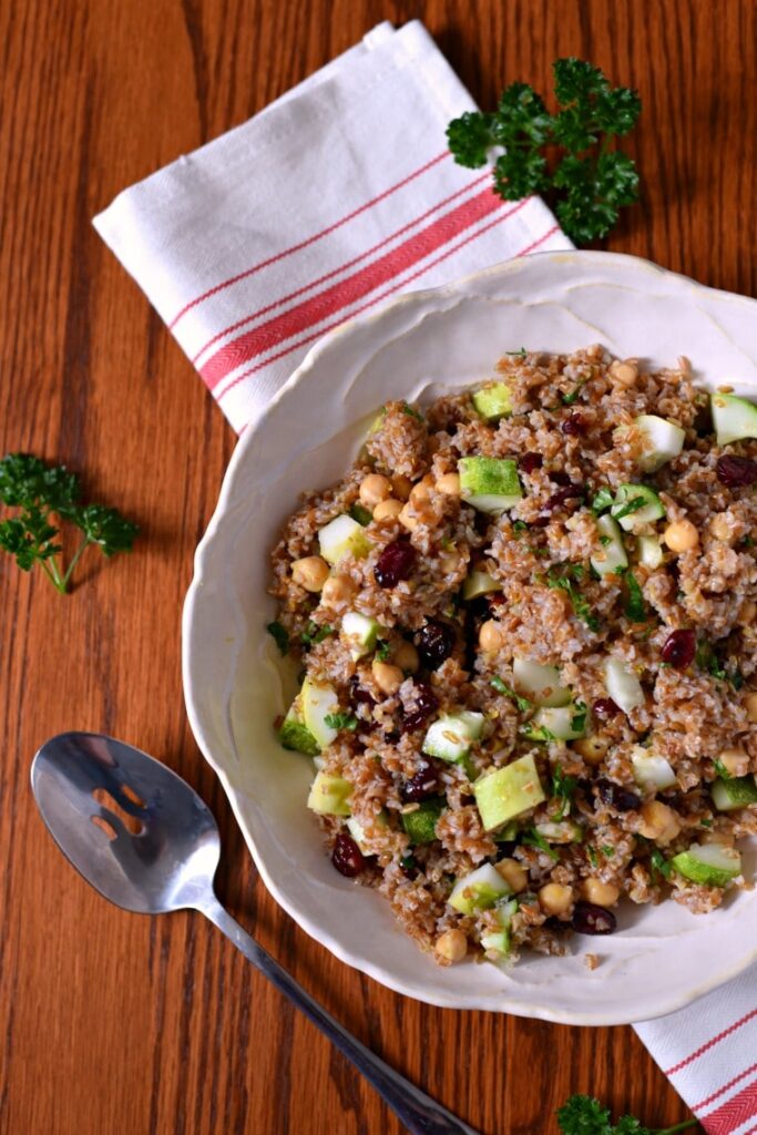 A white serving bowl of bulgur salad on a wooden table