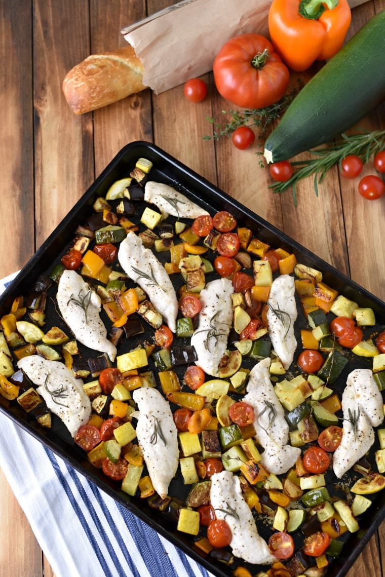 A sheet pan on a wooden table with ratatouille and rosemary chicken tenders 