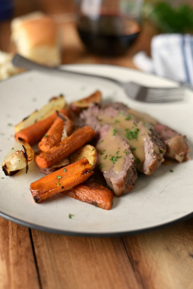 A white plate with sliced roast beef and roasted veggies