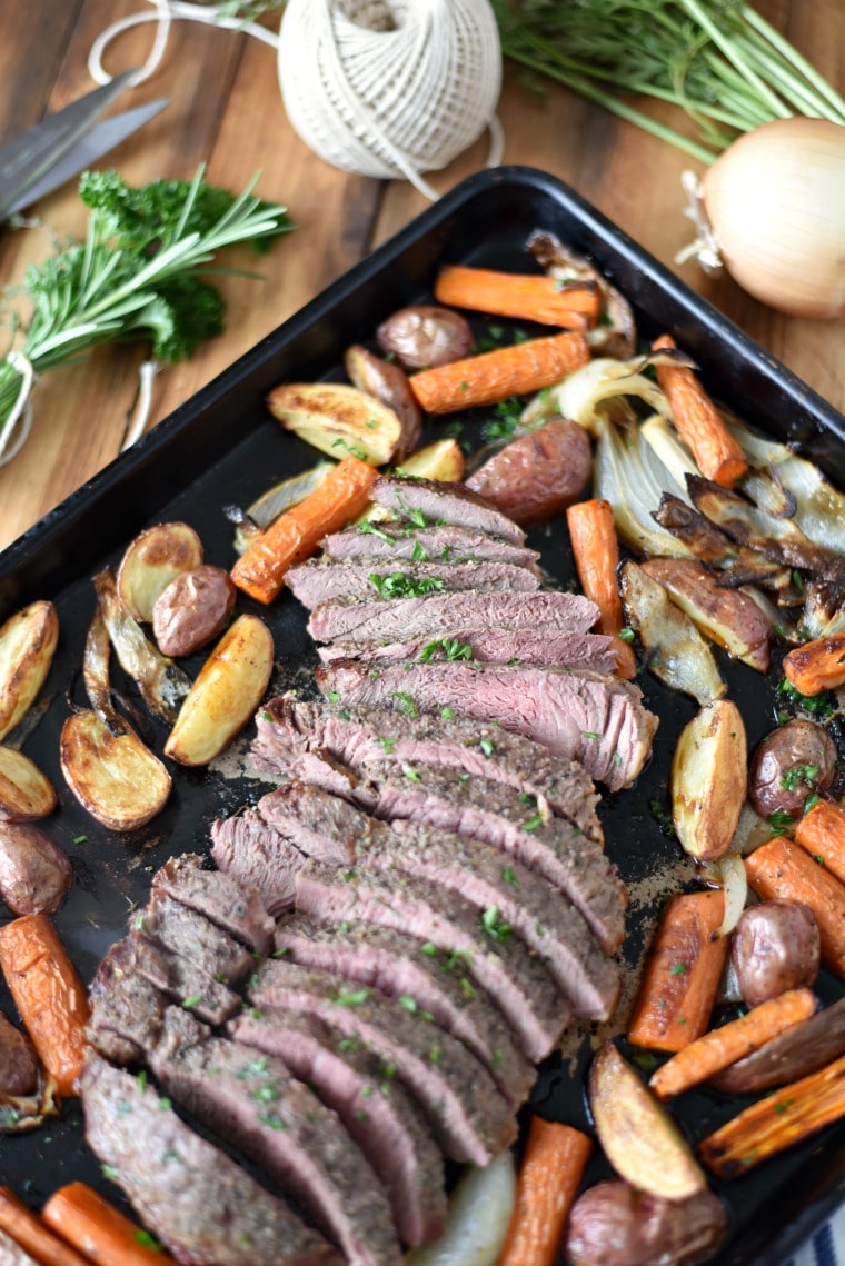 A baking sheet with roasted carrots, onions, and potatoes, with sliced roasted steak 