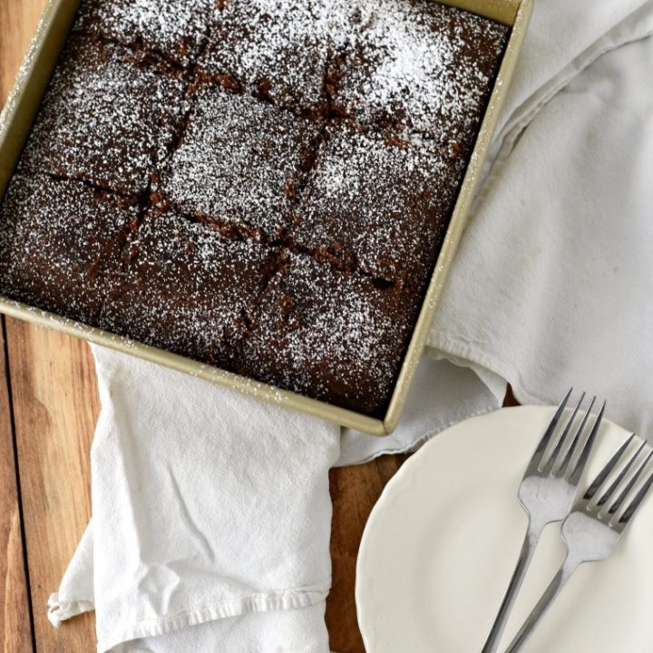 A pan of colonial gingerbread cake on a white napkin and a white plate with 2 forks beside