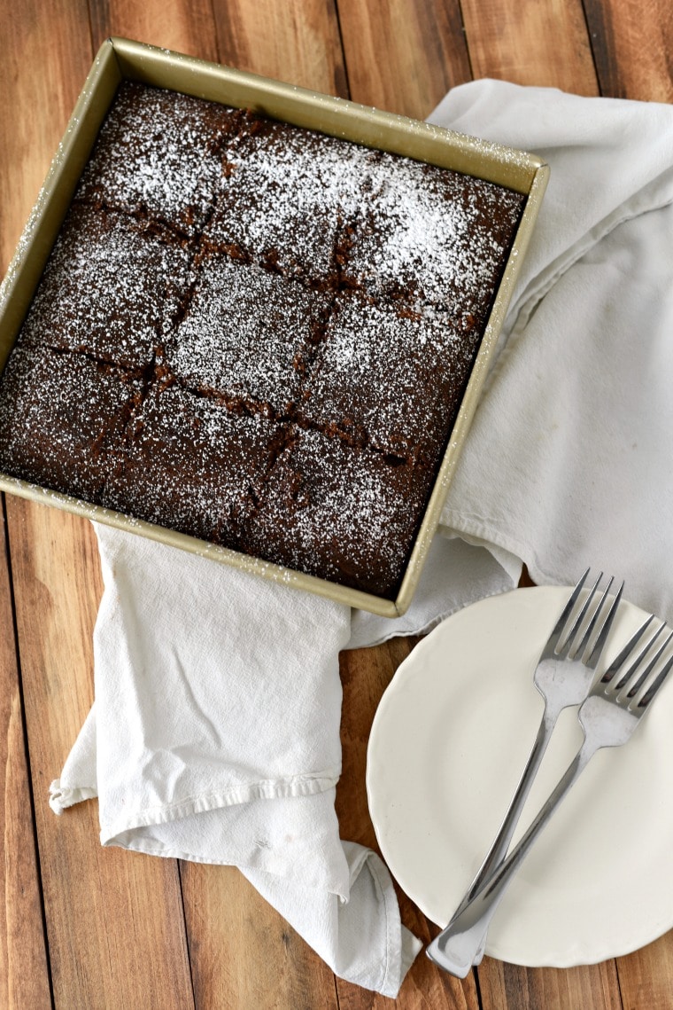 A pan of colonial gingerbread cake on a white napkin and a white plate with 2 forks beside