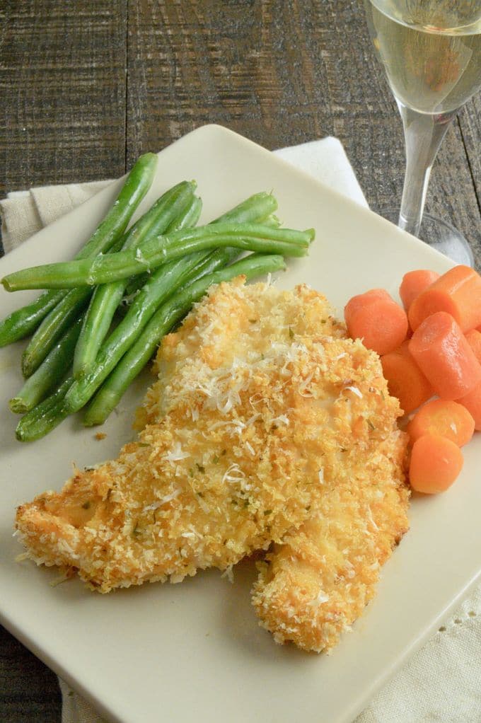 A white plate with green beans, breaded chicken tenders, and carrots.