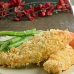 Breaded chicken tenders with green beans and carrots on a white plate with branches of red flowers in the background