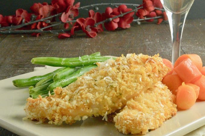 Breaded chicken tenders with green beans and carrots on a white plate with branches of red flowers in the background