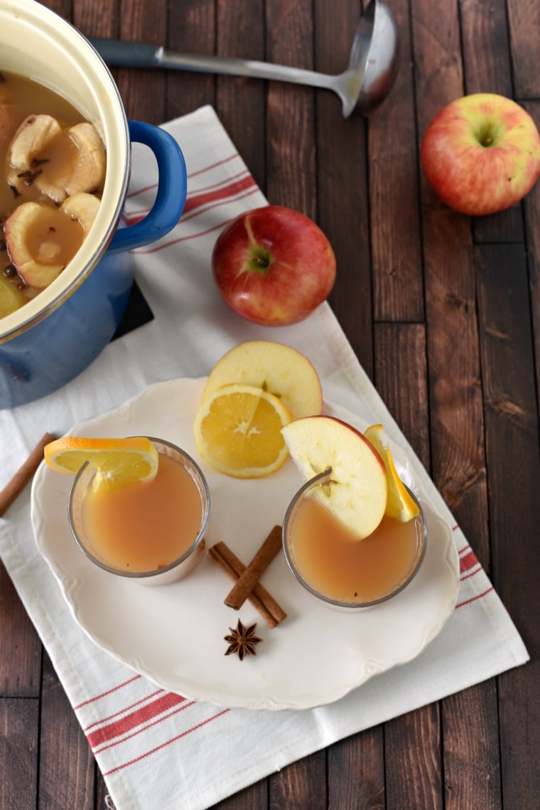 A white plate with two glasses and a blue stock pot full of apple cider wassail.