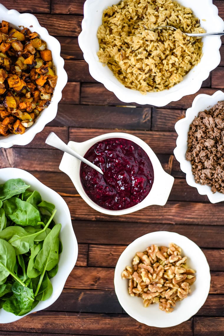 table with bowls of rice, roasted vegetables, spinach, walnuts, berry sauce and ground bison.