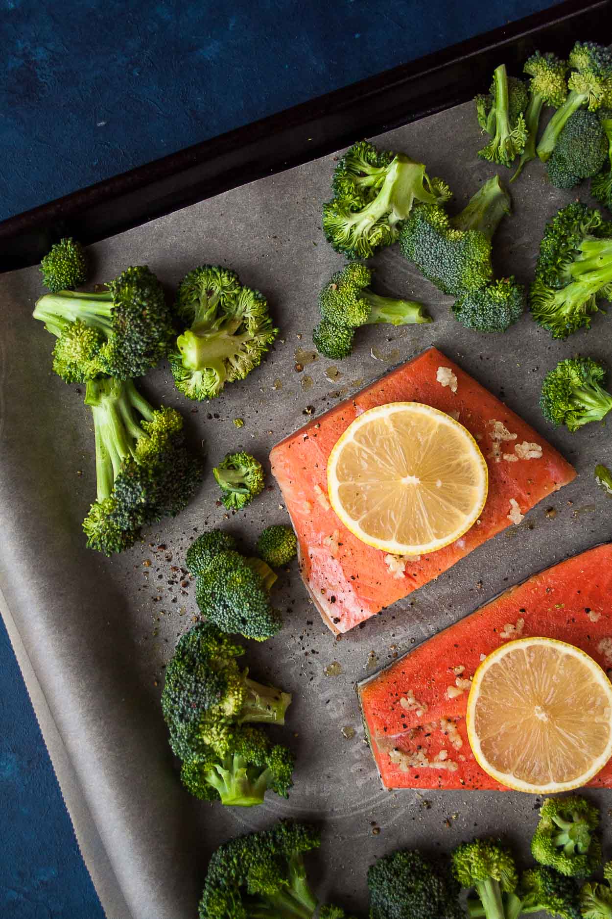 Roasted broccoli and two salmon fillets with lemon slices on a pan with parchment paper