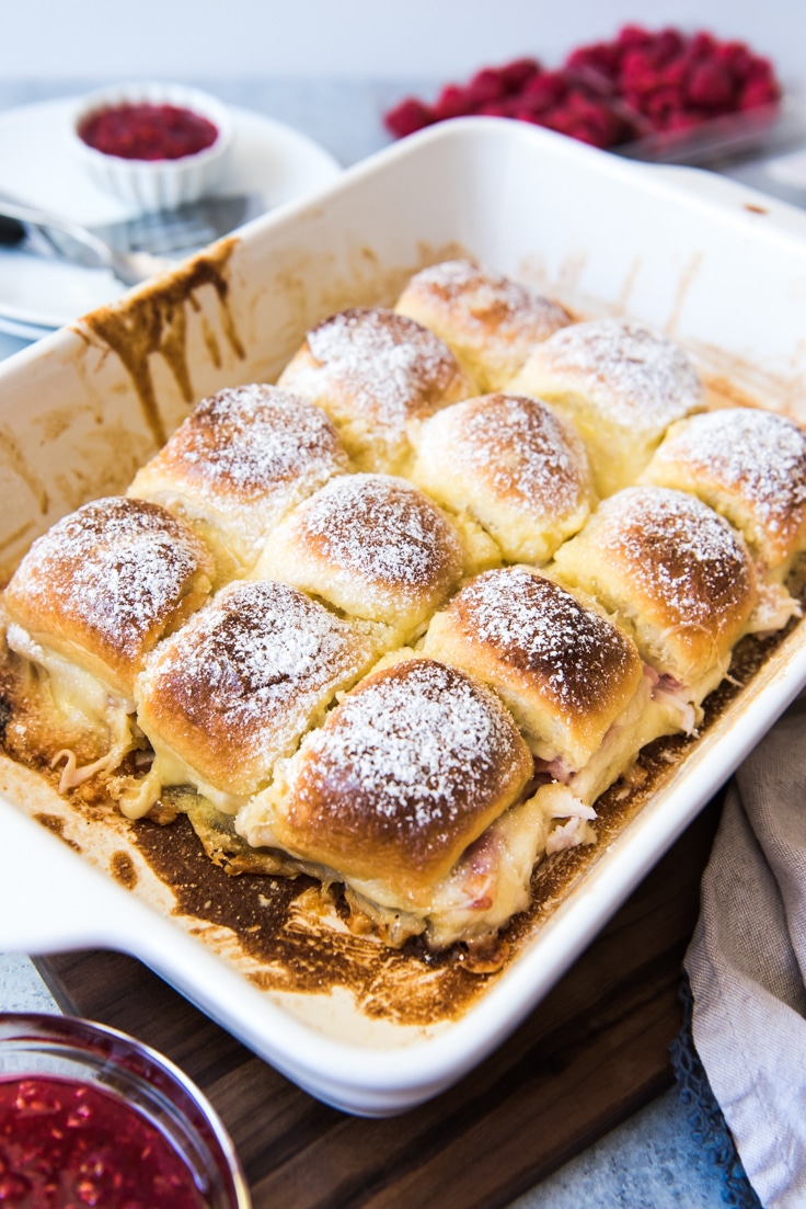 A baking dish filled with 12 monte cristo sliders dusted in powered sugar 