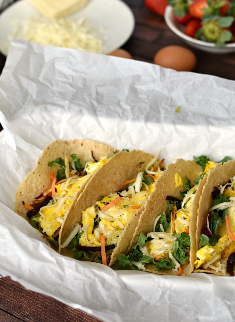 Four breakfast tacos on a white plate with parchment paper