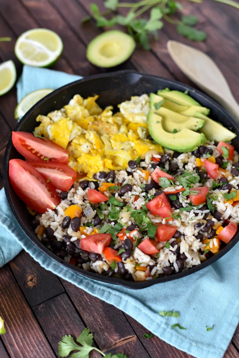 A cast iron skillet filled with gallo pinto: a rice and beans dish with tomatos, eggs, and avocado