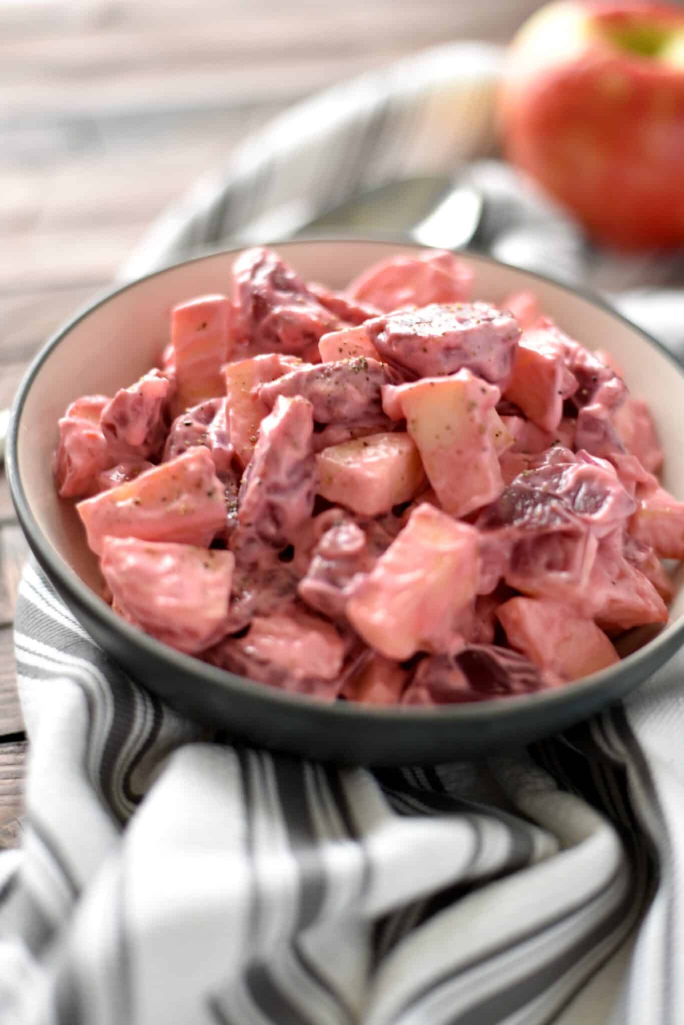 A bowl with beet and apple salad sitting on a black and white striped towel