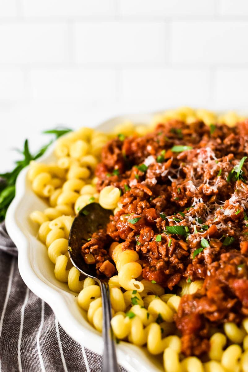 white platter with pasta and beef ragu with serving spoon on the side