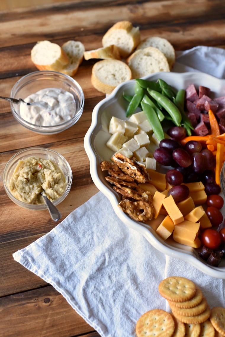 A charcuterie plate on a wooden table with two bowls of dips and spreads next to it