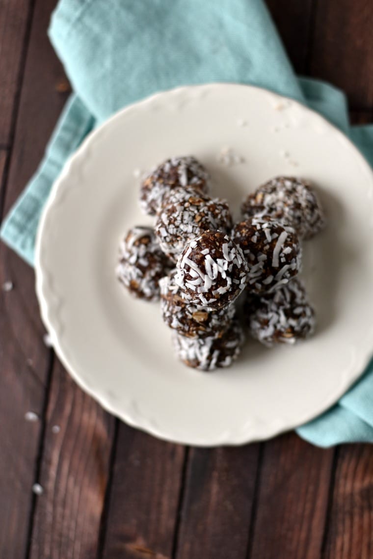 A pile of chocolate coconut ball cookies on a white plate which is sitting on a blue napkin on a wooden table
