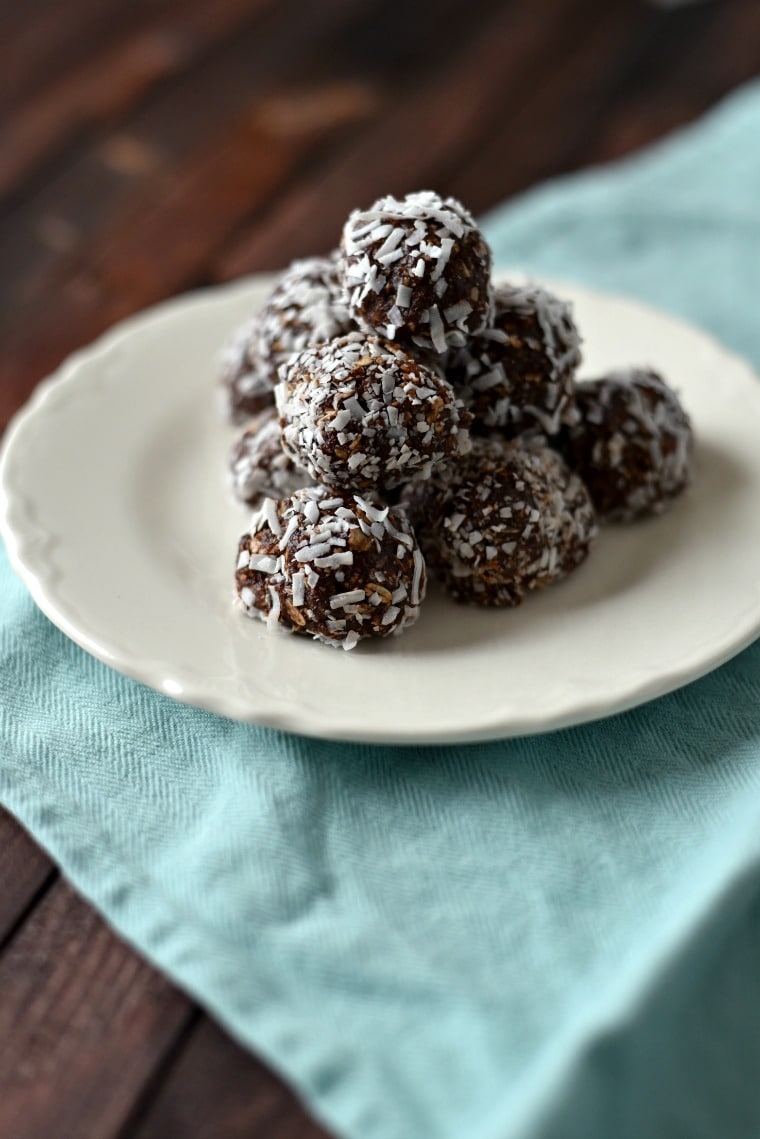 A pile of chocolate coconut ball cookies on a white plate sitting on a blue napkin