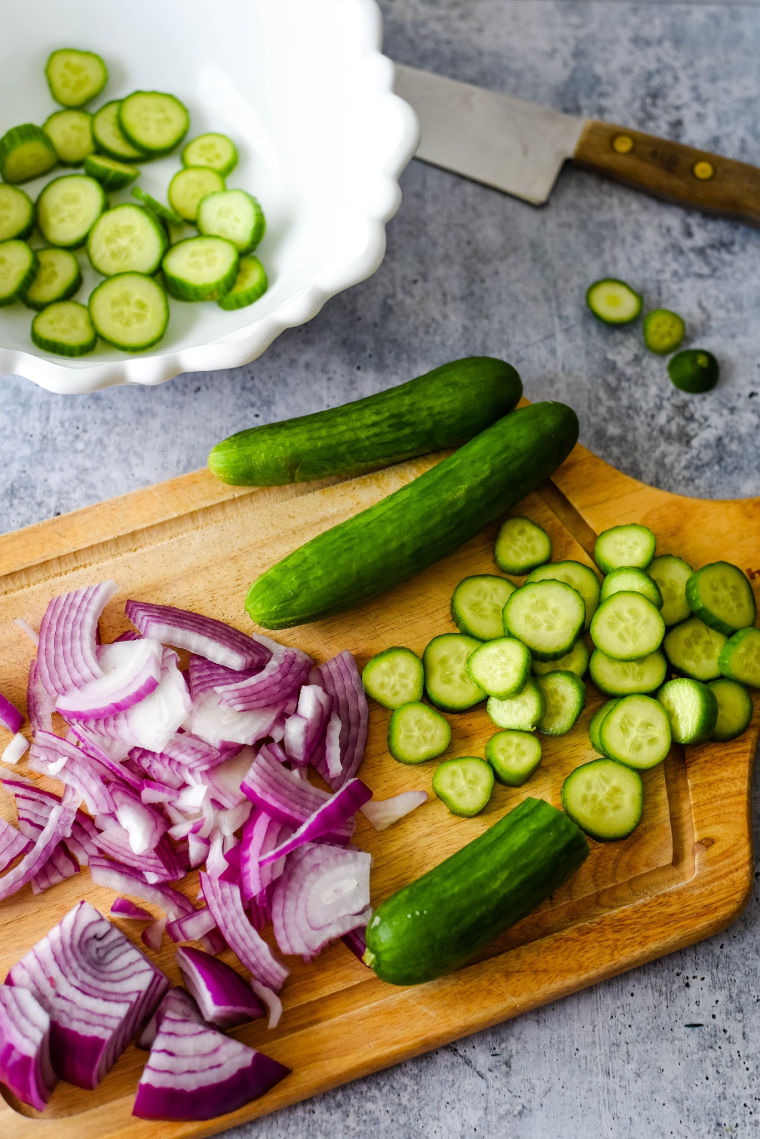cucumbers and red onion sliced on wooden cutting board
