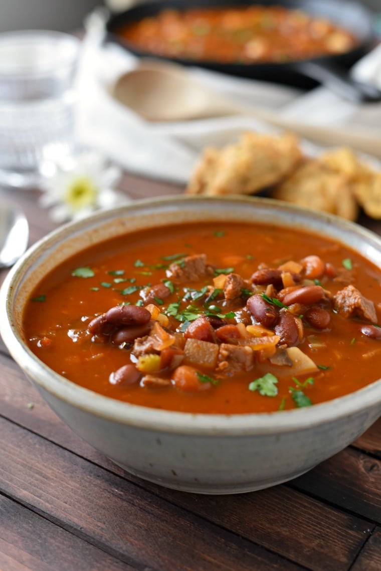 Goulash in a white bowl on a wooden table with biscuits and daisies in the background