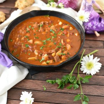 A cast iron skillet full of goulash with a Rapunzel doll in the background and daisies and herbs in the foreground