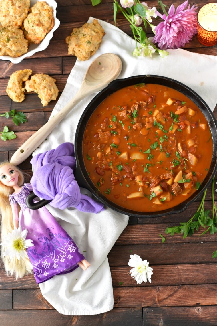 Goulash in a cast iron skillet with a Rapunzel doll and a wooden spoon next to it