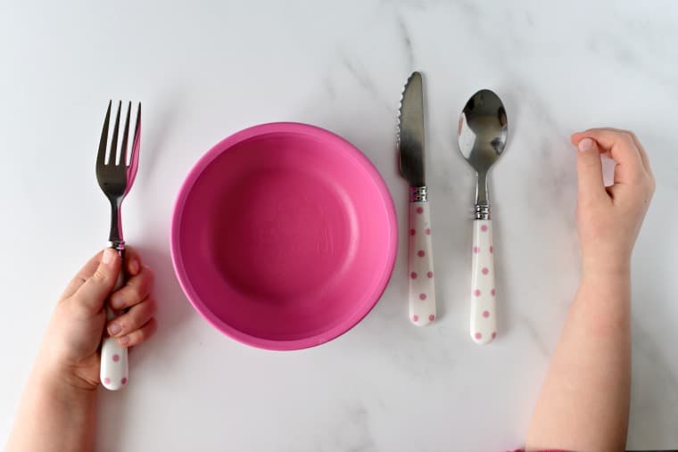 child\'s hands beside pink bowl, and child sized silverware set