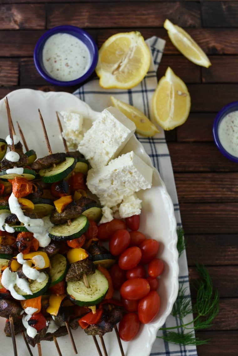 beef souvlaki skewers on plate with lemon wedges, feta, and tzatziki sauce