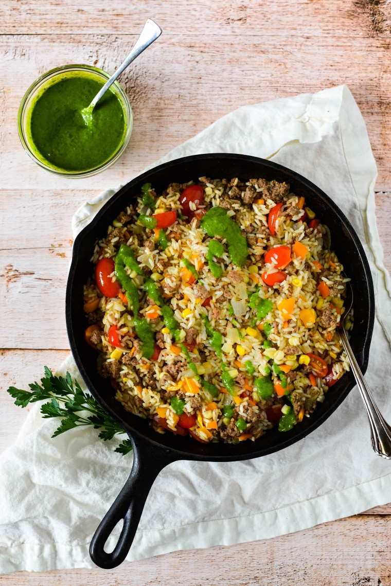 Cast iron skillet with ground beef and rice drizzled in chimichurri sauce