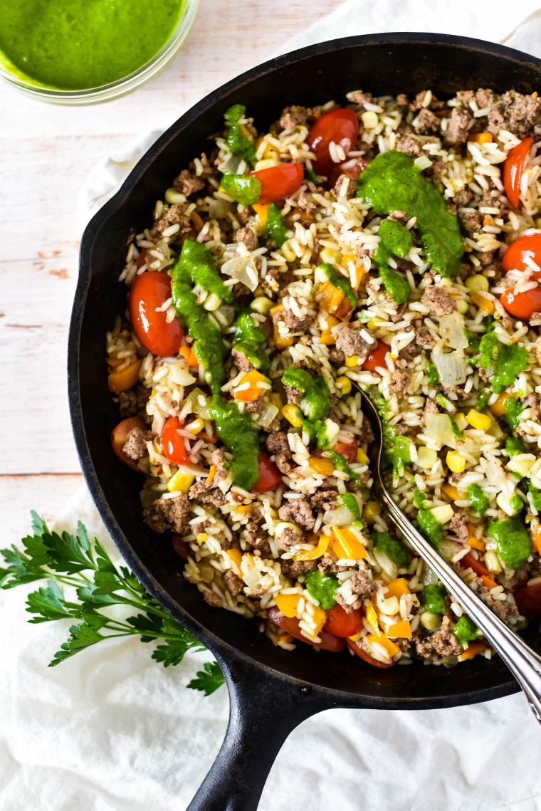 cast iron skillet with ground beef and rice and chimichurri sauce