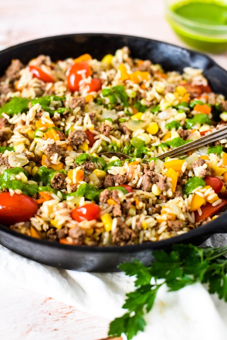 skillet with ground beef and rice with chimichurri sauce in background